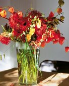 Close-up of red gerbera, Chinese lantern flower, grasses and berries in glass vase