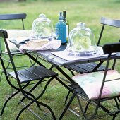 Elegant table setting with glass bell jars, folding chairs and table in garden