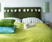 weiße Katze liegt auf Bett, grünes Kopfteil mit Rosen, Kissen