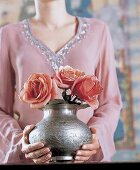 Frau hält eine Blumenvase mit drei Rosen in ihren Händen