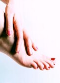 Close-up of woman's hand and foot wearing nail polish against white background