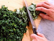 Close-up of man chopping spinach on wooden cutting board