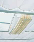 Faltrollos aus hellem Stoff unter Dachverglasung an Spannseilen
