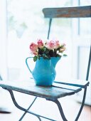 Rosenstrauß steht in einer blauen Kanne auf einem Holzstuhl