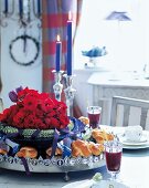 Close-up of roses with snacks in tray and lit candlesticks on table set for Christmas