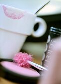 Close-up of compact powder, brush, accessories and a cup with lipstick mark on it