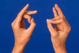 Close- up of woman's hand performing acupressure mudra against blue background