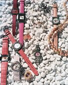Various watches and jewellery scattered on pebbles stone