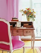 Flowers in glass jar on wooden desk with photo frame and pink chair