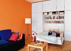 Klappbett aus weißem Wandschrank, Beistelltisch aus Holz, Wand orange