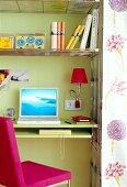 Laptop and books on green shelf with pink chair in small home office