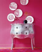 Silver chest with vase and plates as wall hanging on pink wall