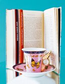 Close-up of coffee cup with butterfly print kept in front of open book with bookmark