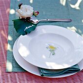 Geschirr mit Blumenmuster auf grüner Serviette, Rosenblatt als Platzkarte