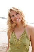 Portrait of beautiful blonde woman wearing green halter top standing on beach, smiling