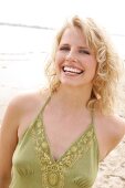 Portrait of beautiful blonde woman wearing green halter top standing on beach, smiling