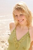 Portrait of beautiful blonde woman wearing green halter top standing on beach, smiling