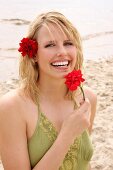 Woman wearing green halterneck dress holding red flower on beach, laughing