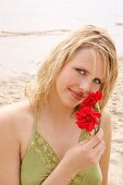 Woman wearing green halterneck dress holding red flower on beach, laughing