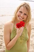 Woman wearing green halterneck dress holding red flower on beach, laughing