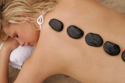 Rear view of blonde woman lying on beach with stones on her back