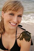 Portrait of beautiful woman in black bikini top sitting with seaweed on shoulder, smiling