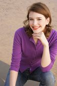 Portrait of beautiful woman wearing purple sweater and jeans sitting on beach, smiling
