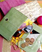 Close-up of green snake leather handbag with mirror, coins and sunglasses