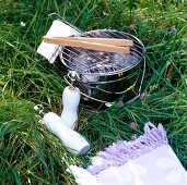 Portable stainless steel grill bucket with wooden tongs on grass