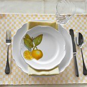 Teller mit Zitrusmotiv, Besteck, Glas auf Karo-Tischset weiß-gelb