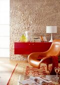 Helle Steinoptik-Wand, rotes Lack- sideboard, Ledersessel, Teppich.