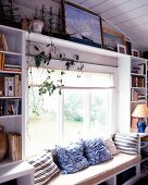 Cosy bench with cushions in front of window and beside bookshelves in living room