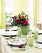 Laid out table with green glasses and decorated with various flowers in green flower vase