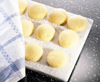 Round yellow dough in row with cloth on floured board