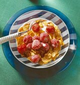 Close-up of cornflakes with strawberries in striped bowl with a spoon