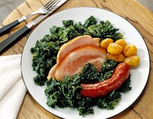 Kale with cooked sausage, smoked pork, pork cheek and roast potatoes on plate