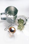 Steel measuring cup and glass container with liquid and steel strainer on white background