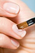 Hand einer Frau, Fingernagel wird mit Gel bestrichen