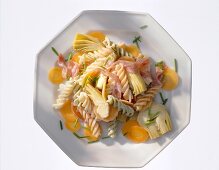 Pasta salad with artichokes, carrots and ham on plate, overhead view