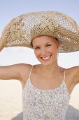 Portrait of cheerful woman wearing floral pattern dress and big straw hat on beach