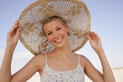 Portrait of cheerful woman wearing floral pattern dress and big straw hat on beach