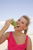 Portrait of blonde woman holding bunch of grapes and eating, smiling