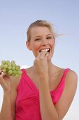 Portrait of blonde woman holding bunch of grapes and eating, smiling