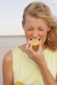 Blonde woman biting into slice of lemon and grimacing