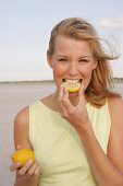 Blonde woman biting into slice of lemon and grimacing