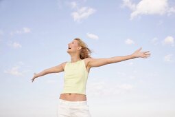 Happy woman with windswept hair with arms outstretched, looking up and laughing