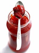Glass jar of strawberry and rhubarb jam with spoon on it