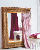 Goldener Wandspiegel steht mit rosanem Kleid behängt auf dem Boden