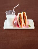 Vegetable sandwich and glass of milk with straw on serving dish