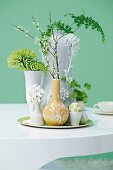 Verschiedene Vasen mit Blütenzweigen und Osterdeko auf dem Tisch